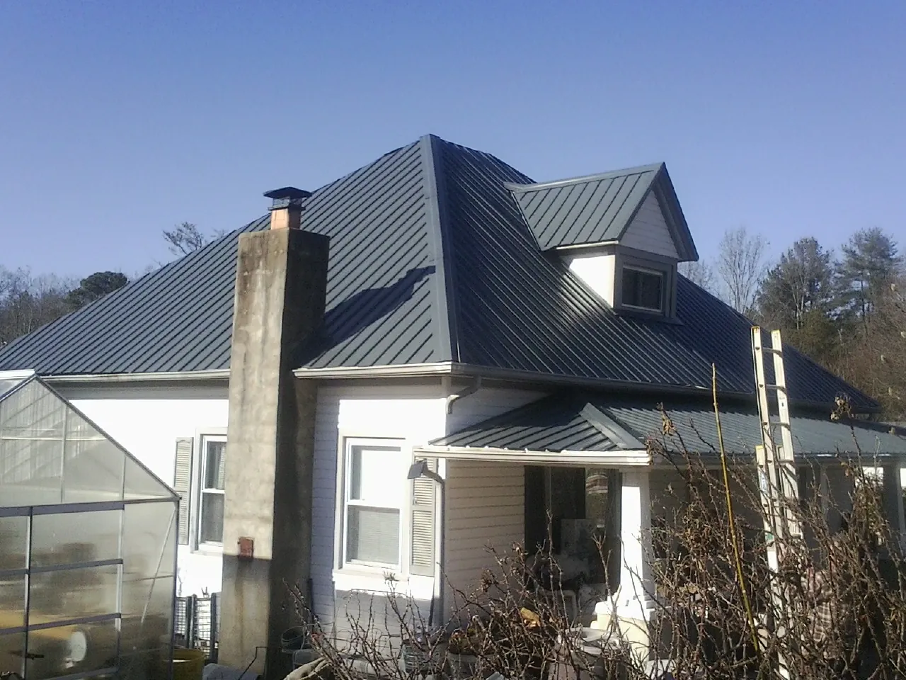 Dark blue standing seam metal roof on a white farmhouse with dormer — Slate & Tile Roof Repair by Roofing Brothers in Hedgesville