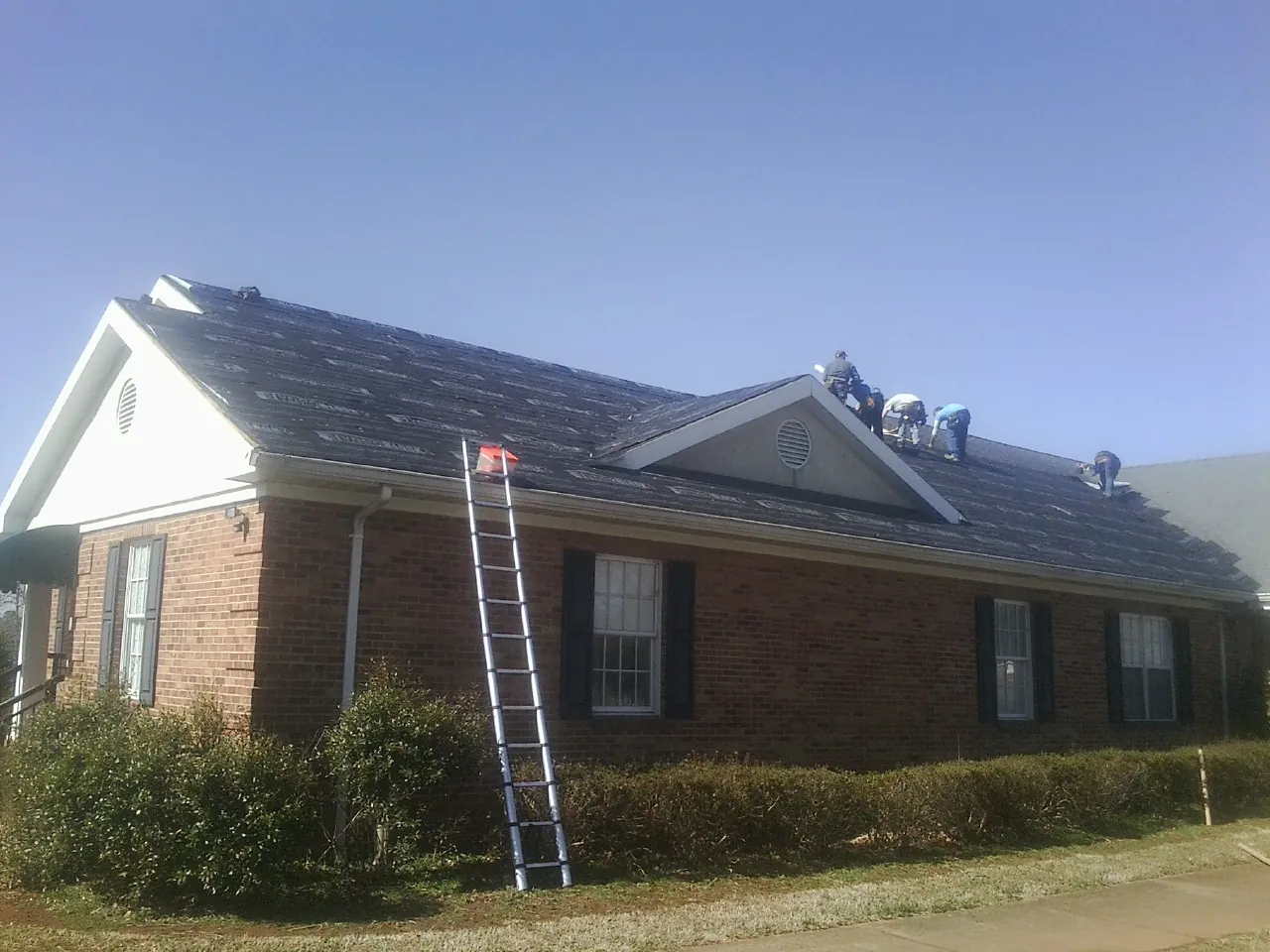 Crew tearing shingles off a brick ranch roof with a ladder set — Emergency Roof Repair work by our crew in Hedgesville