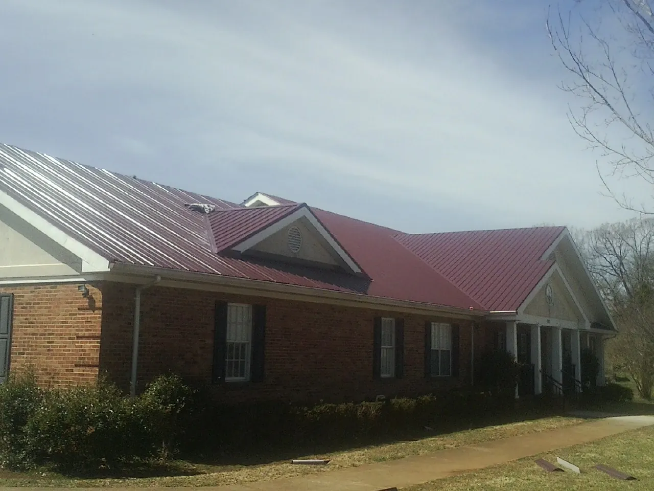 Red metal roof with gabled entries on a long brick building, from a Hail Damage Roof Repair job in Hedgesville