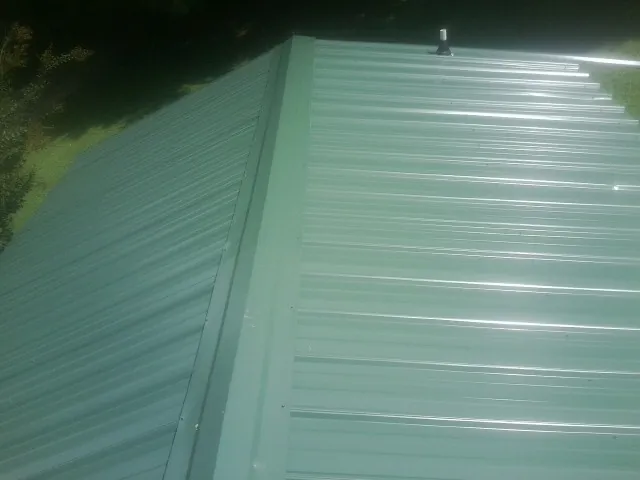 New green metal panels meeting at the ridge of a roof — Flat Roof Repair work by our crew in Hedgesville