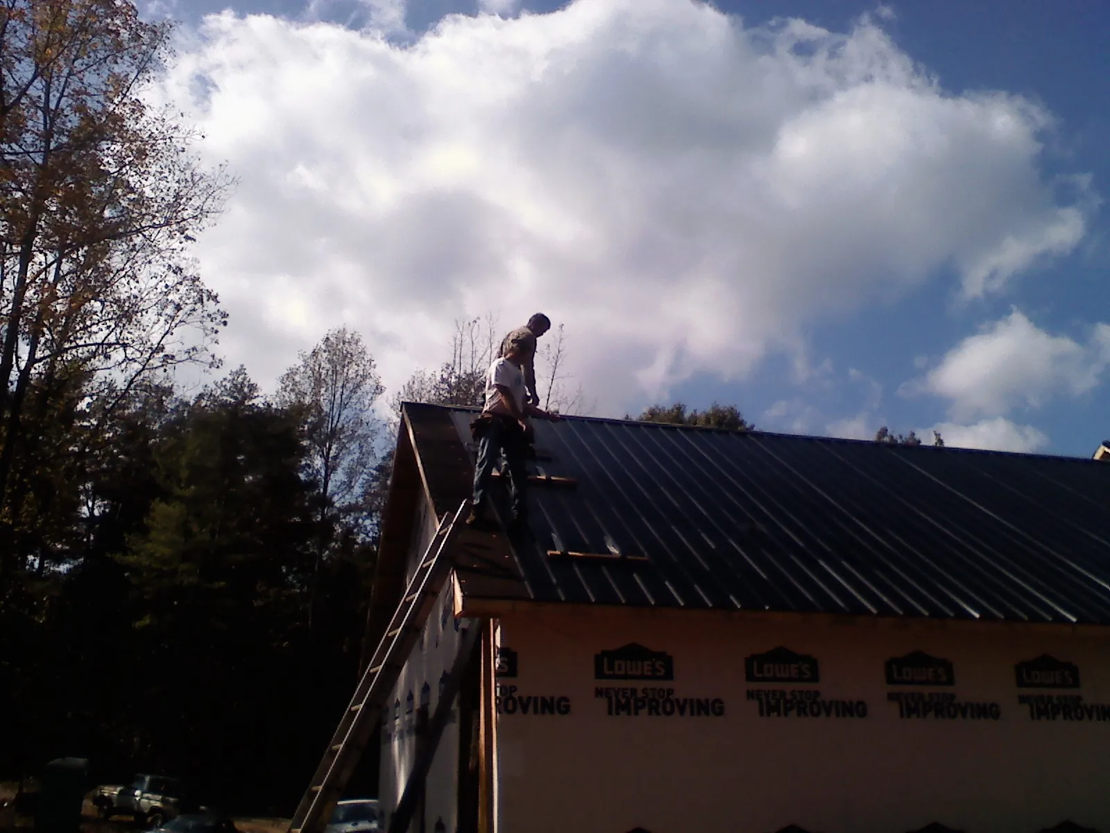 Roofer fastening dark metal panels high against a cloudy sky, from a Roof Inspection job in Hedgesville