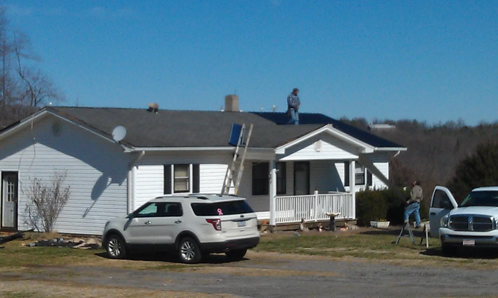 Roofers stripping shingles from a white ranch house roof in Hedgesville