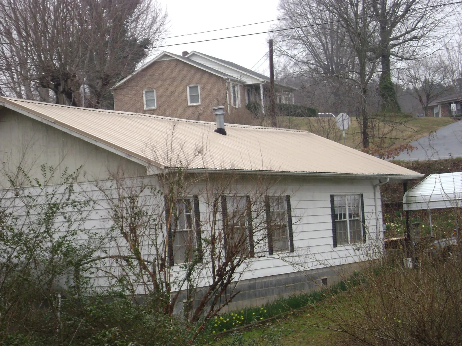 Tan metal roof on a white sided house set into a hillside — Commercial Roofing by Roofing Brothers in Hedgesville